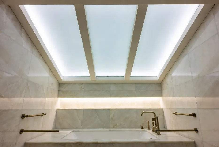 Frosted glass backlit false ceiling design in a luxury bathroom with marble tiles and soft lighting.