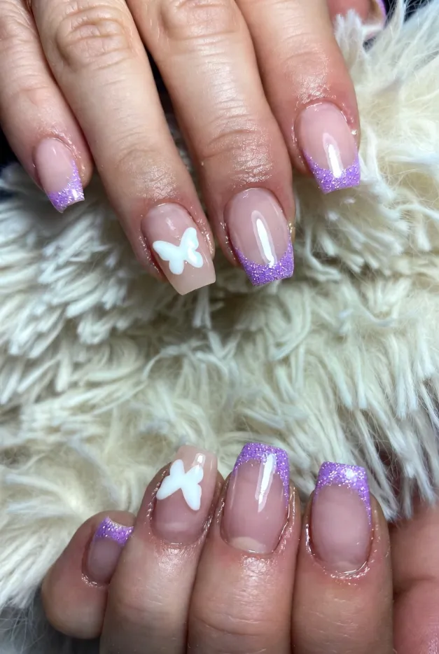 Lavender glitter French tip nails with a sheer pink base and butterfly accents for a dreamy summer manicure.