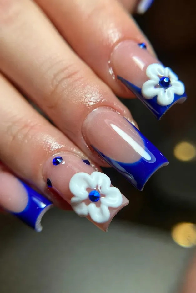 3D floral French tip nails with blue tips, rhinestones, and raised flowers for a luxury summer nail design.
