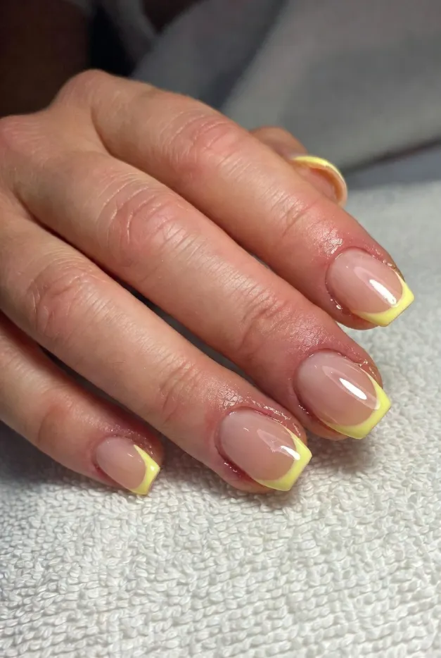 Short lemon yellow French tip nails with a nude glossy base for a cheerful summer nail design in 2026.