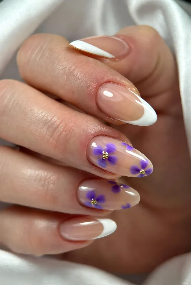 White French tip nails with lavender flower accents and glossy almond shape for a romantic summer manicure.
