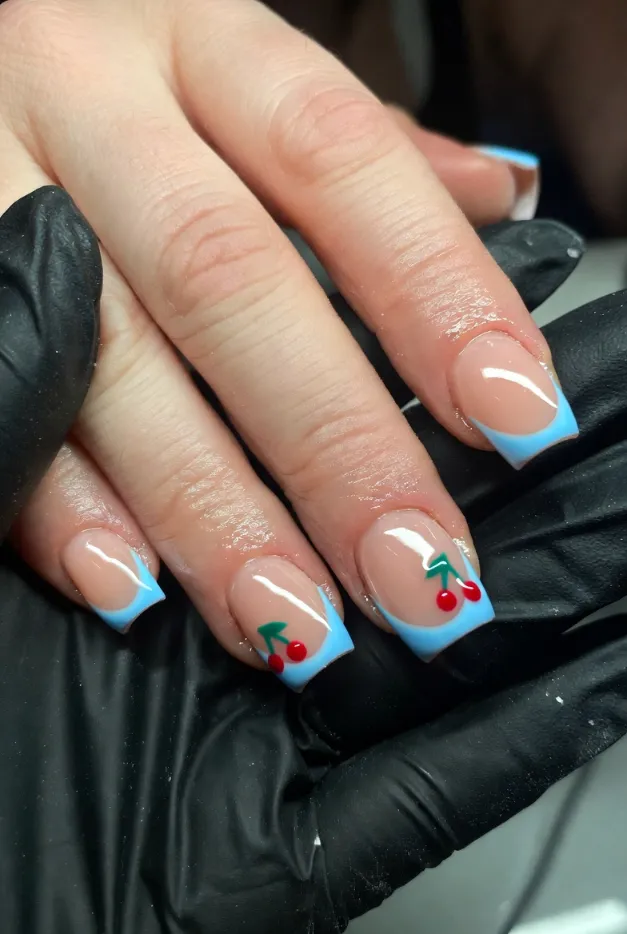 Baby blue French tip nails with tiny cherry accents on short square nails for a cute summer nail idea.