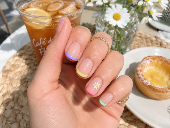 Short June nails with pastel French tips and a tiny daisy accent design.
